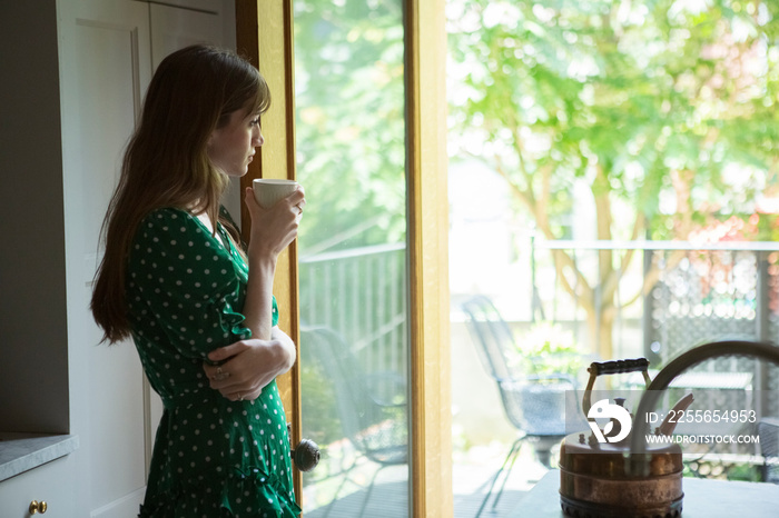 Thoughtful woman holding tea cup looking through doorway at home