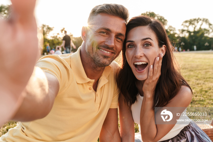 Portrait delighted middle-aged couple taking selfie photo and smiling while sitting in summer park