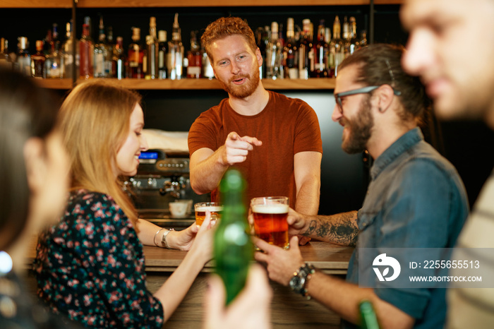 Young handsome barman talking with customers. Pub interior.