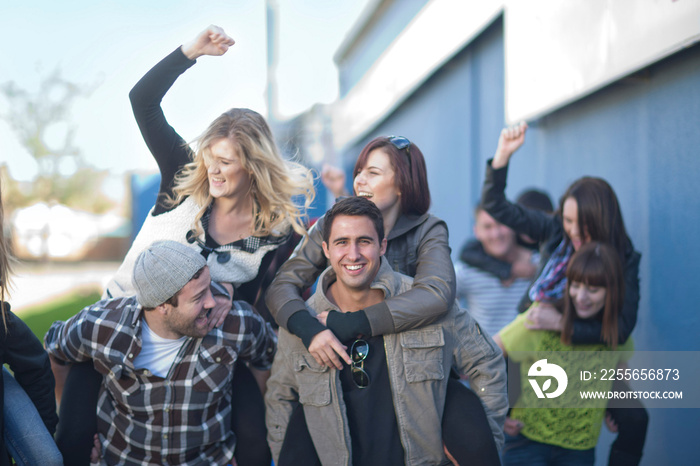 Group of young adults having piggy back race