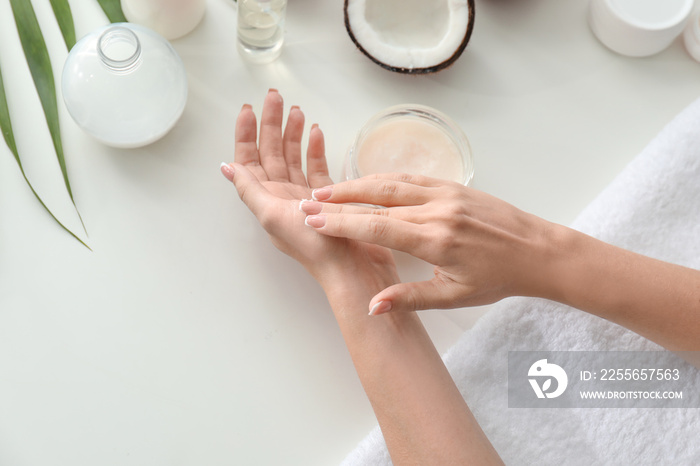 Woman applying coconut oil onto skin at white table