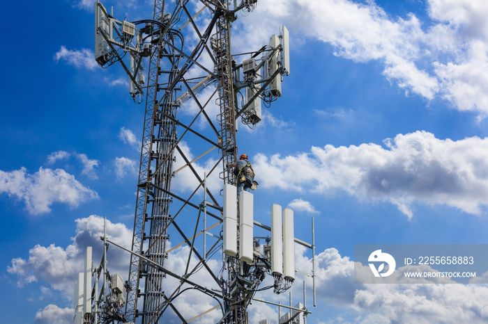 Telecom maintenance. Man climber on tower against blue cloudy sky background.