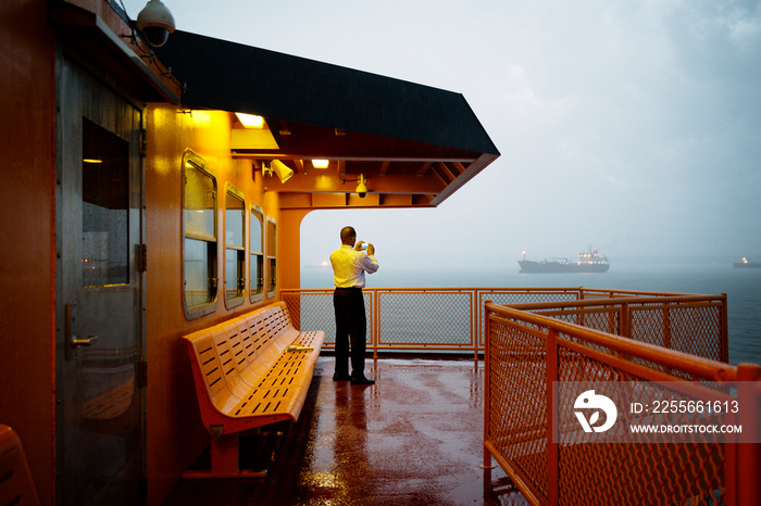 Rear view of man taking picture with smartphone while standing on ferry