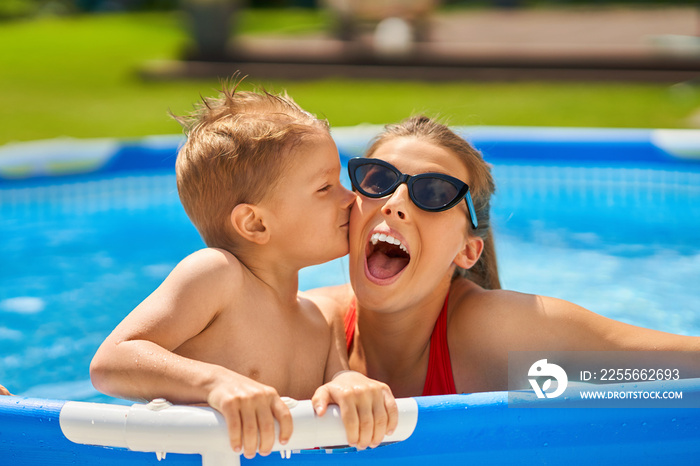 Cute boy with his mother playing in swimming pool during summer