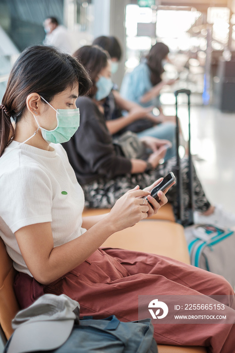 Young female wearing face mask and using mobile smartphone in airport, protection Coronavirus diseas