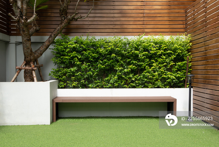 Outdoor green grass artificial garden with long wooden bench wooden wall, backyard patio.