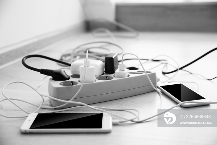 Mobile phones charging into power cord on wooden floor indoors