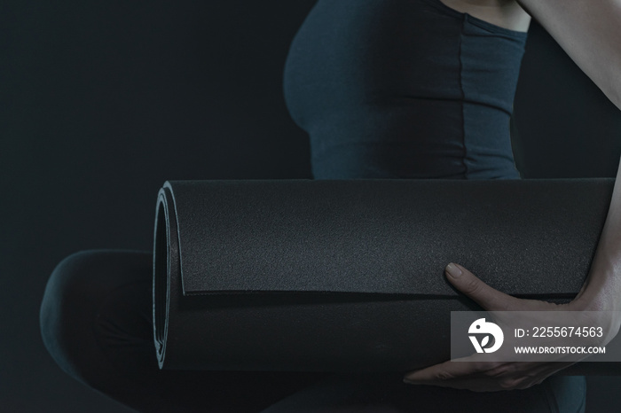 Young woman with yoga mat practicing yoga on dark black background. close up