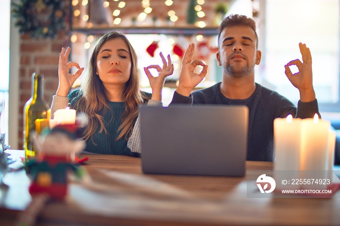 Young beautiful couple sitting using laptop around christmas decoration at home relax and smiling wi