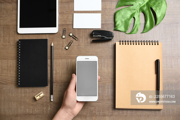 Woman holding phone over table with stationery. Mockup for design