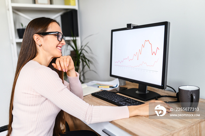 Young woman is using PC for work from home office, woman in eyeglasses looks at computer screen with