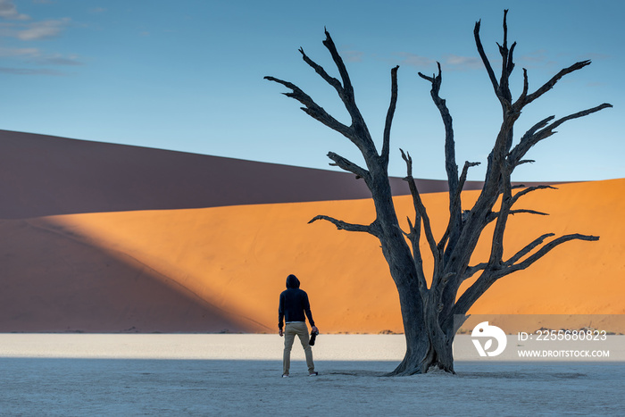 Young man photographer and traveler standing between dead trees in deadvlei (Sossusvlei) during sunr