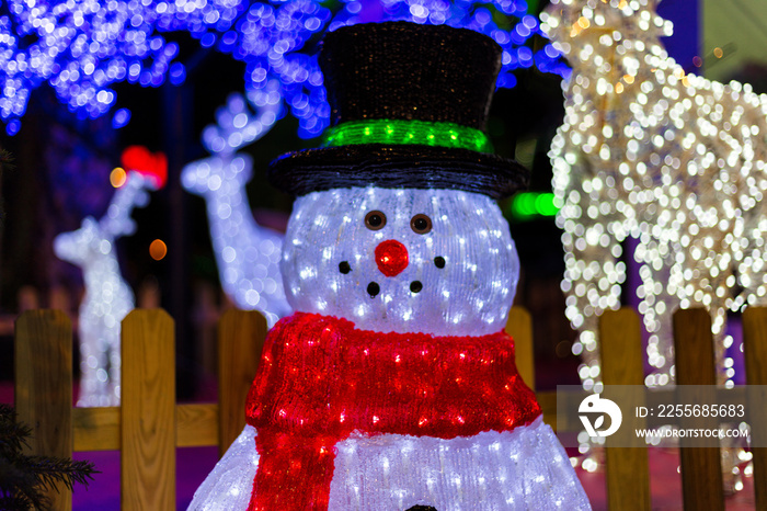 Christmas decoration with LED illuminated figures. A lit snowman with hat and red scarf. In the back