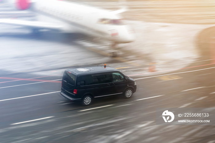 Black VIP service van running on airport taxiway with blurred private jet on background. Business cl