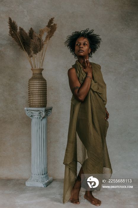 full body portrait of African American Canadian woman with afro wearing green toga next to roman col