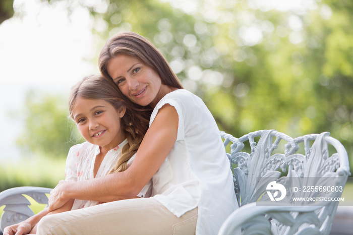 Portrait affectionate mother hugging daughter on bench in garden