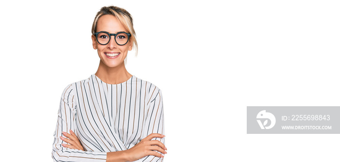 Beautiful blonde woman wearing business shirt and glasses happy face smiling with crossed arms looki