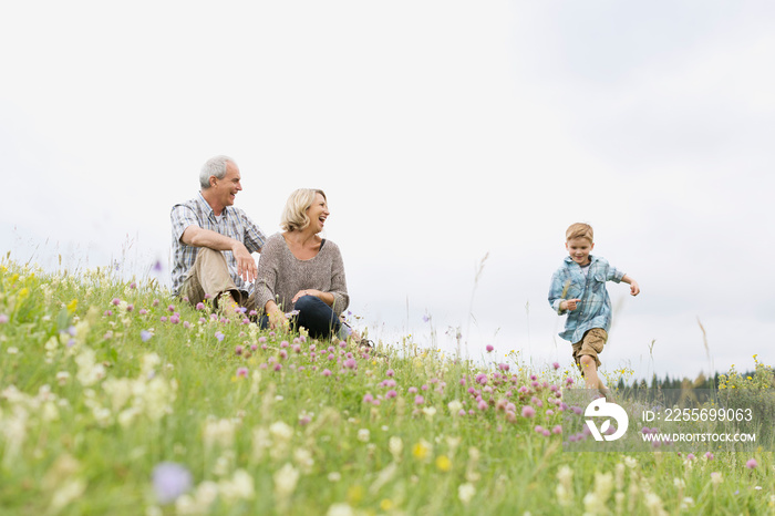 Grandparents watching grandson run in meadow