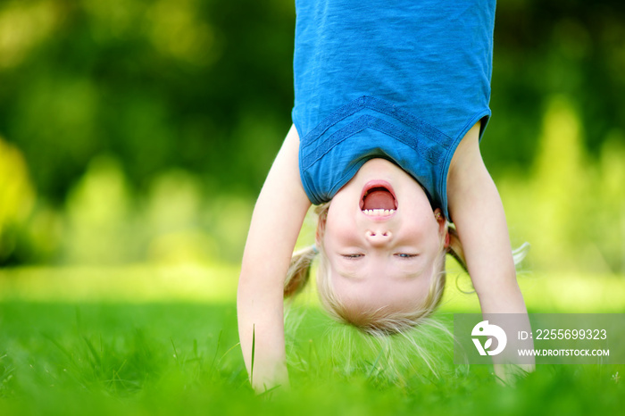 Happy young child playing head over heels on green grass