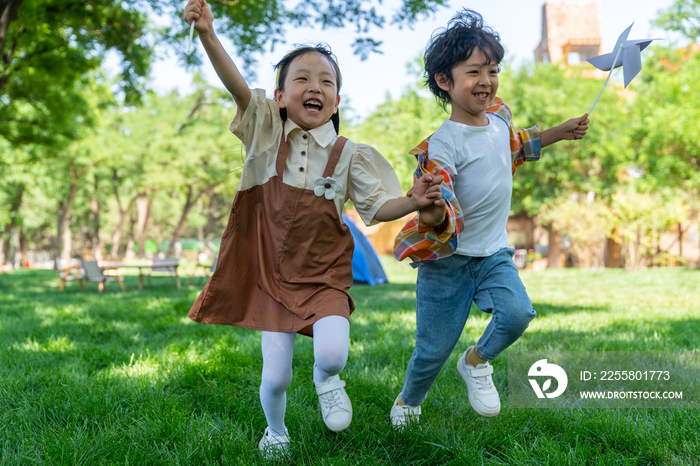 两个小孩子在草地上举着风车开心奔跑