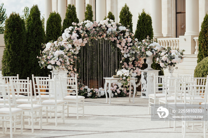 Beautiful modern round wedding arch for unique luxury wedding ceremony with fresh flowers. White chairs near.