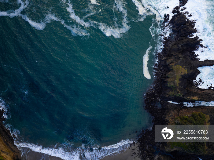 Shot from the air. Dark blue ocean surface with light white waves and rocky shore with green moss. Beautiful seascape. The beauty of nature, calm scenes, ecology, geography, geology.