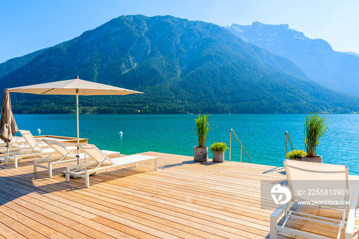 Pier with chairs on sunny terrace on shore of beautiful Achensee lake on sunny summer day with blue sky, Karwendel mountain range, Tirol, Austria