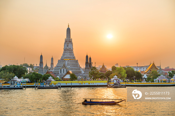 Temple of Dawn or Wat Arun and boats on Chao Phraya River at sunset with shining sun. Bangkok, Thailand