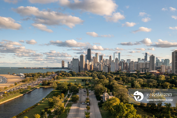 Beautiful view of the downtown Chicago skyline from above a linear parking lot between South Lagoon and South Pond in Lincoln Park near the zoo with green trees below and blue sky above.