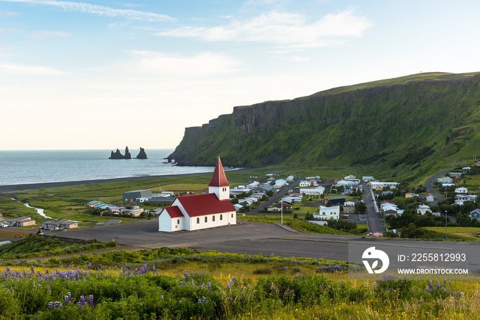 Beautiful view of the coastal town of Vik in Iceland in summer. A small church with a red roof is visible in foreground.