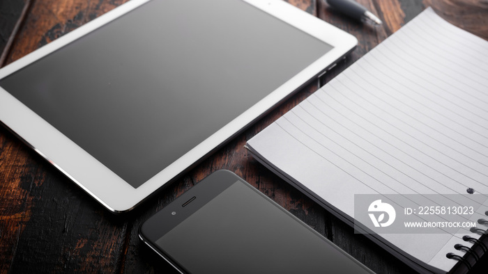 digital tablet, smartphone and notebook on wooden background, view on a desktop.