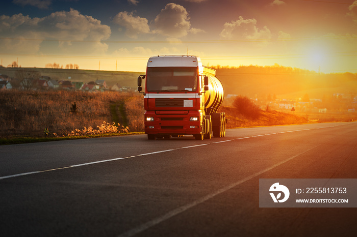 Arriving red truck on the road in a rural landscape at sunset