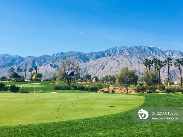 A beautiful practice area in Palm Springs, California, United States.  The chipping green has a bunch of golf balls by the hole and the beautiful San Bernardino Mountains in the background.