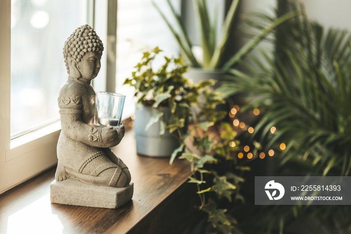 Buddha statue close-up in beautiful light. Close up of a Buddha figurine. Modern decor on a shelf, a buddha and a candle holder and a plants in a pot. Spiritual awakening