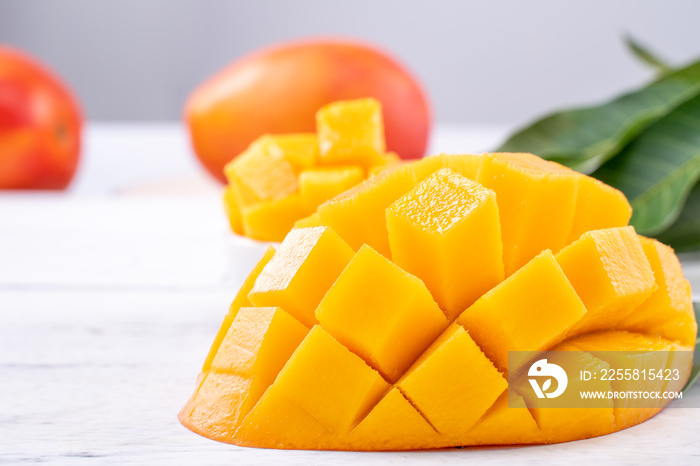 Fresh mango,beautiful chopped fruit with green leaves on bright wooden table background. Tropical fruit design concept, close up, copy space.