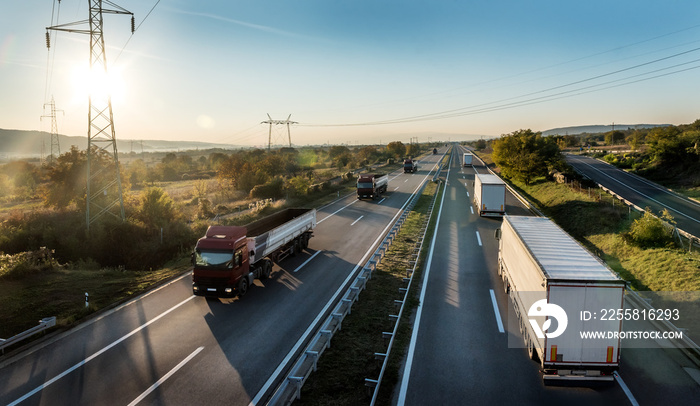 Convoys or caravans of transportation trucks passing on a highway at a beautiful sunset. Transportation And Trucking Industry.