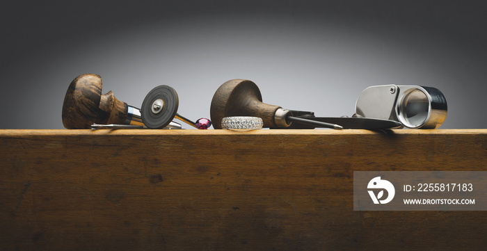 Diamonds golden ring, gem stone, jeweller tools and equipments for jewelry work on an antique wooden desktop on white wall. Jeweller, engraver at work. Horizontal wide concept photo background