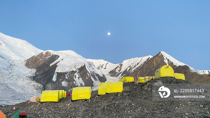 Camp 1 under Lenin Peak with a full moon. View of yellow tents, snow-capped mountains and rocks. Beautiful mountain winter landscape.