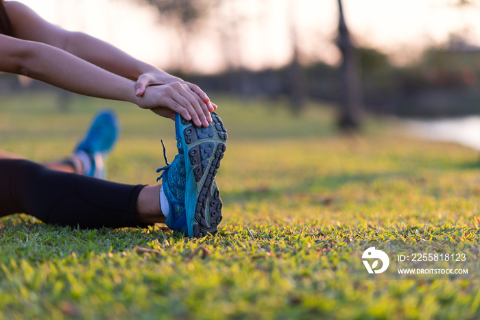 Woman stretching legs in green park at sunset after workout