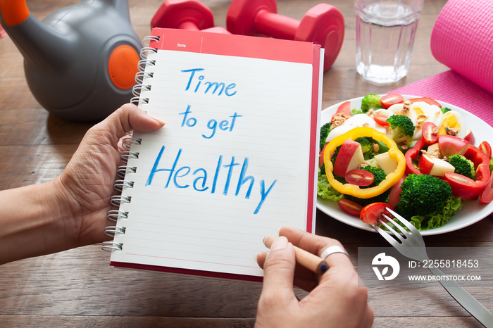 Time to get healthy, text on diary book with salad and fitness items on table. Dieting concept