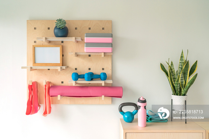 Workout fitness at home gym organized shelves for pilates equipment. Wood pegboard storing resistance bands, weights, yoga blocks, motivational message board. Women exercising at home.