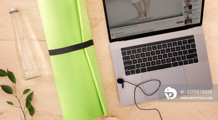 Online sport or training course concept top view Laptop with yoga mat and glass bottle of water on the wood floor