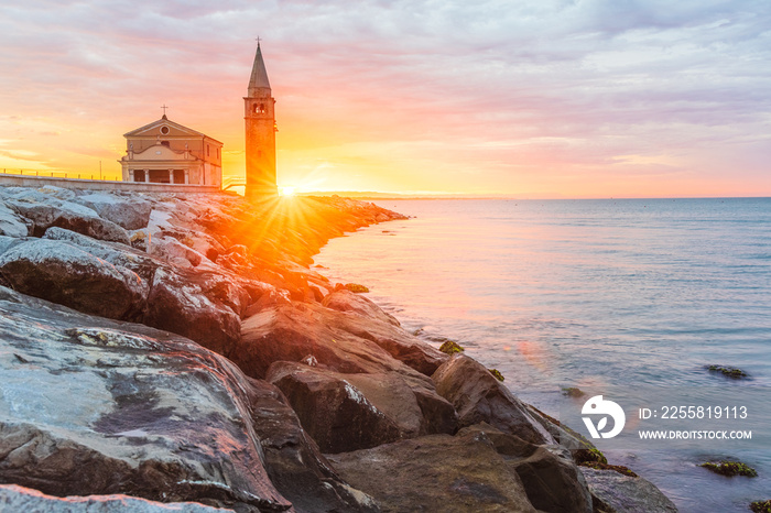 The city of Caorle in Italy at sunrise and its landmark on the main promenade, the Santuario della Madonna dell’Angelo church located right by the sea