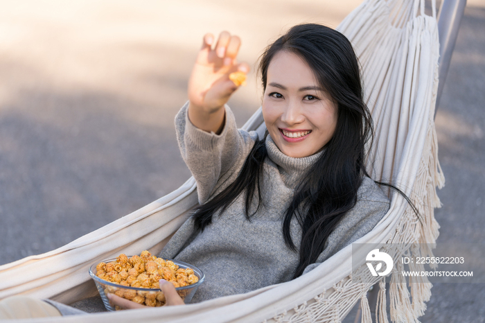 年轻女子坐在吊床上吃爆米花