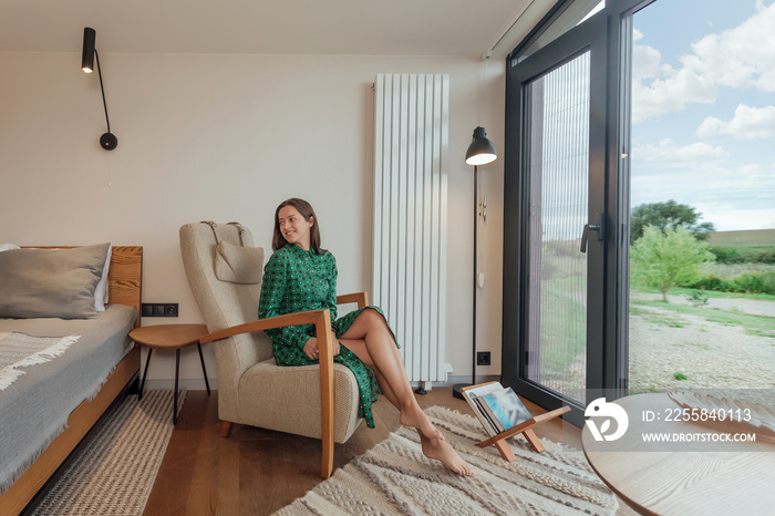 Woman resting in cozy cabin house near window with summer panoramic view