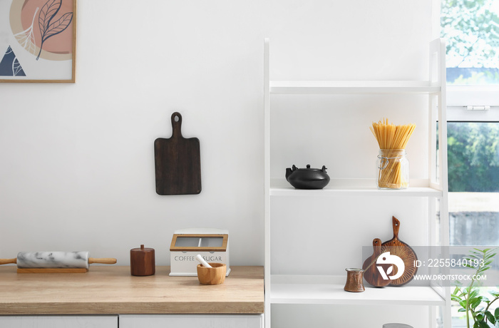 Counter and shelf unit with kitchenware near white wall