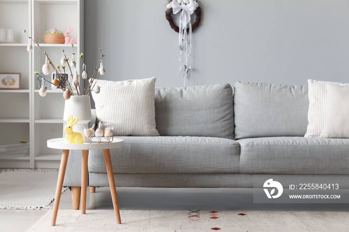 Vase with tree branches, Easter eggs and rabbit on table in interior of living room