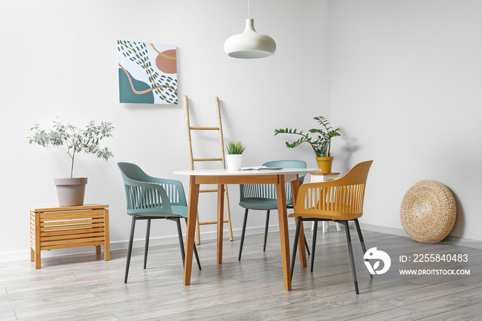 Stylish interior of dining room with modern furniture and houseplants near white wall