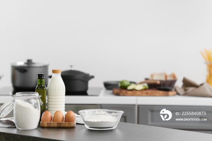 Bowl with flour, eggs and bottle of milk on table in modern kitchen