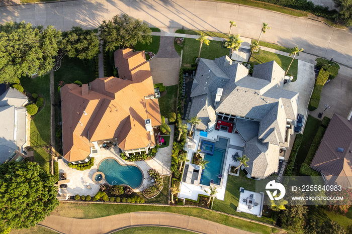 Aerial drone view of luxury mansions with swimming pools surrounded by green grass and trees in the 